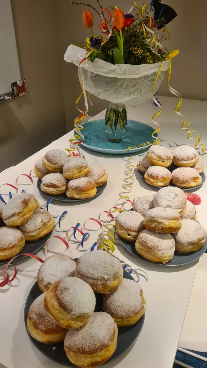 mehrere Teller mit Faschingskrapfen, mit Puderzucker bestäubt, stehen auf einem weißen Tisch, dazwischen sieht man Luftschlangen und dahinter einen Blumenstrauß in einer Vase