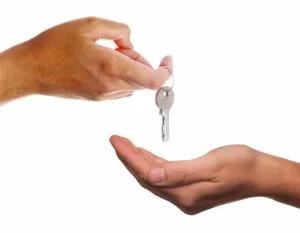 Eine Person hält einen Schlüssel an einem Schlüsselring, eine andere Person hält eine offene Hand unter den Schlüssel